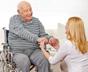 senior man on wheelchair holding caregiver's hands